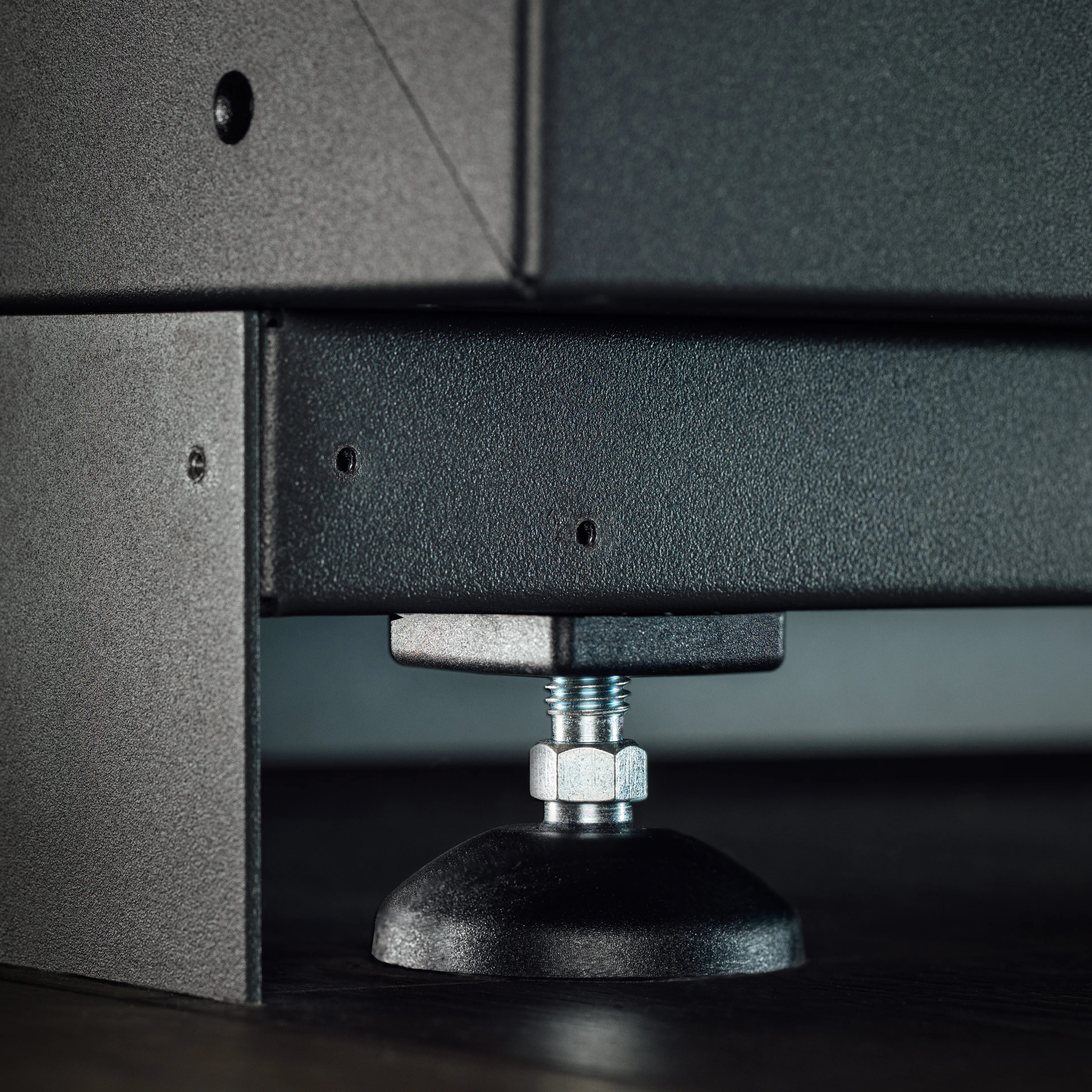 Kick Base Plate image, Close-up of a black metal adjustable leveling foot attached to a piece of furniture, demonstrating its sturdy design and the screw mechanism used for height adjustment. 