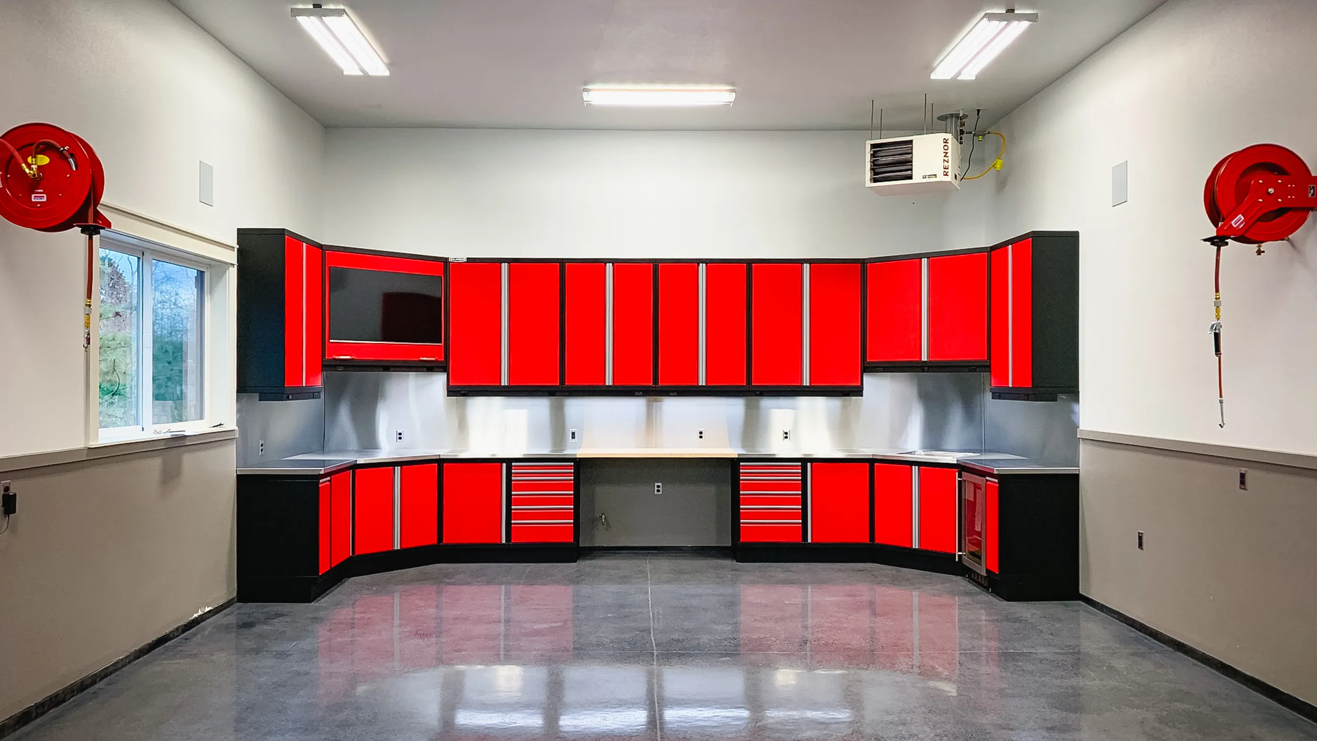 Custom red and black garage cabinets with overhead storage, base drawers, and integrated workspace by Baldhead Cabinets — durable metal cabinet systems for high-end garages and professional workshops