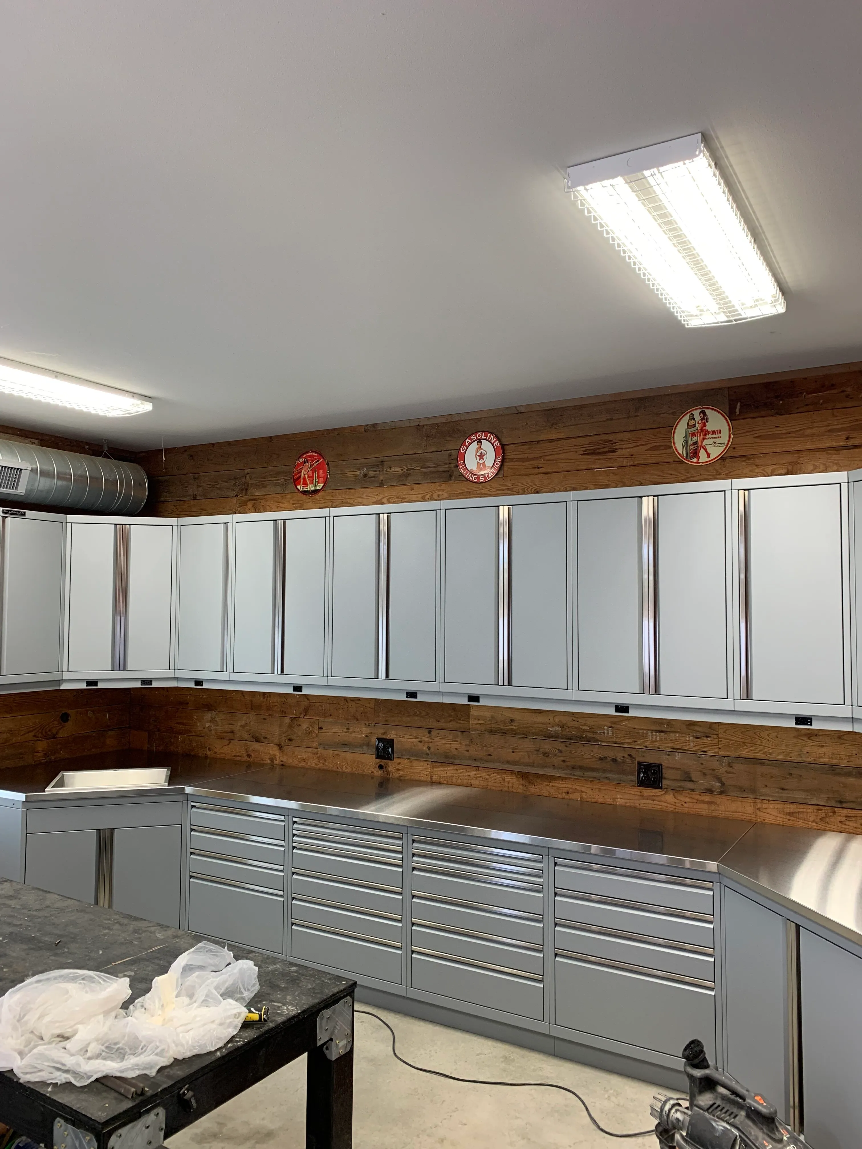 Sleek gray metal garage cabinets with stainless steel countertops and rustic wood accent wall by Baldhead Cabinets — high-quality custom cabinetry for functional and stylish workshop storage solutions