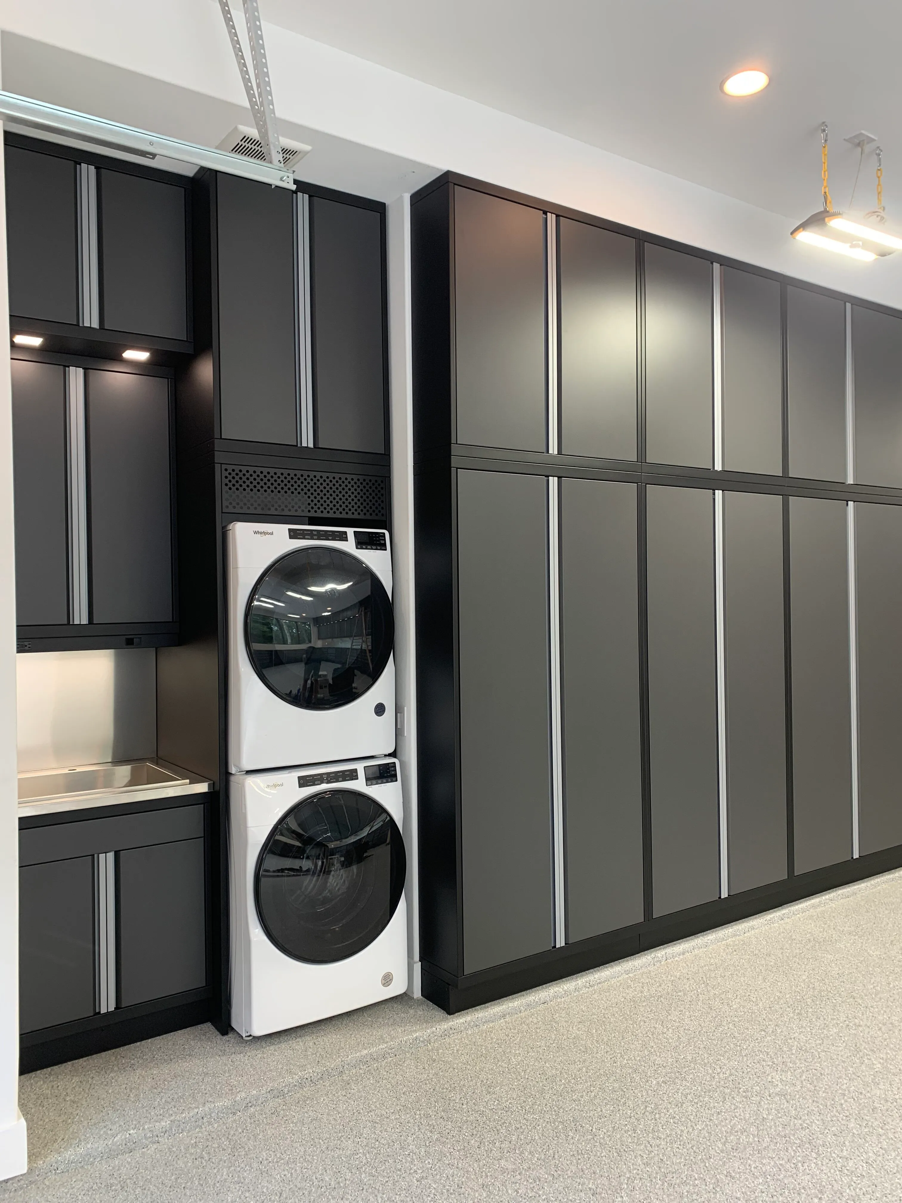 Custom Baldhead Cabinets in matte black finish featuring integrated Whirlpool washer and dryer units, stainless steel utility sink, and full-height storage, ideal for luxury garage laundry organization.