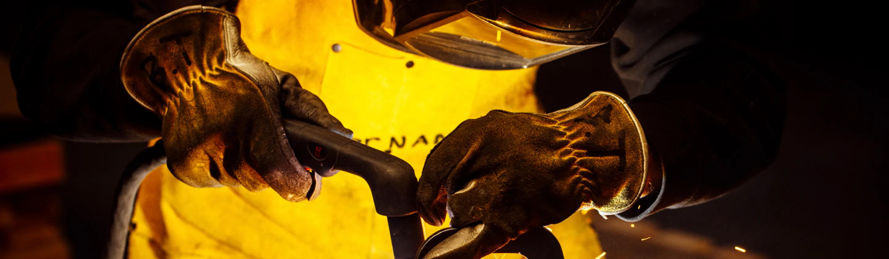 Close-up of a welder's hands in protective gloves, actively engaged in welding, highlighting precision work at Baldhead Cabinets.