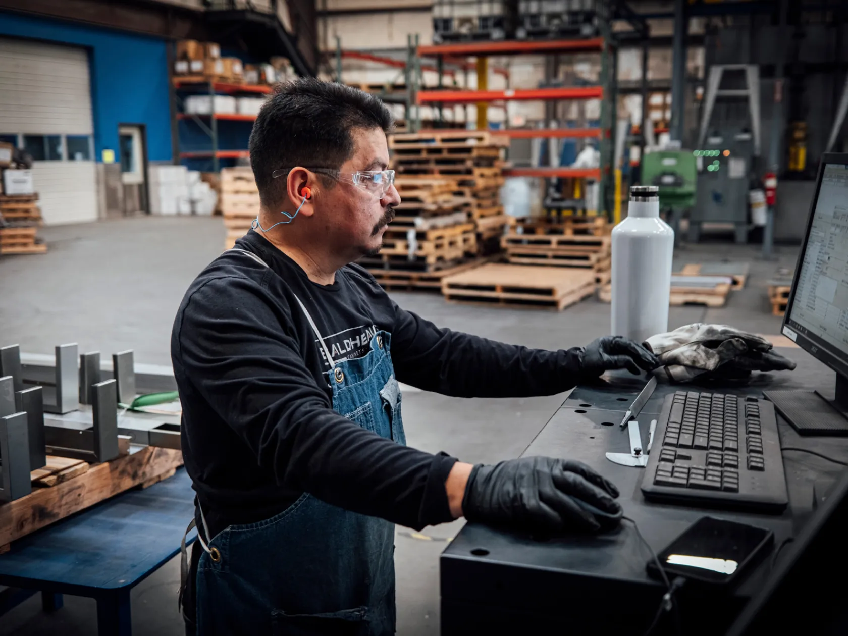 Worker at Bald Head Cabinets using a computer to program CNC machinery for precision metal fabrication in a workshop setting